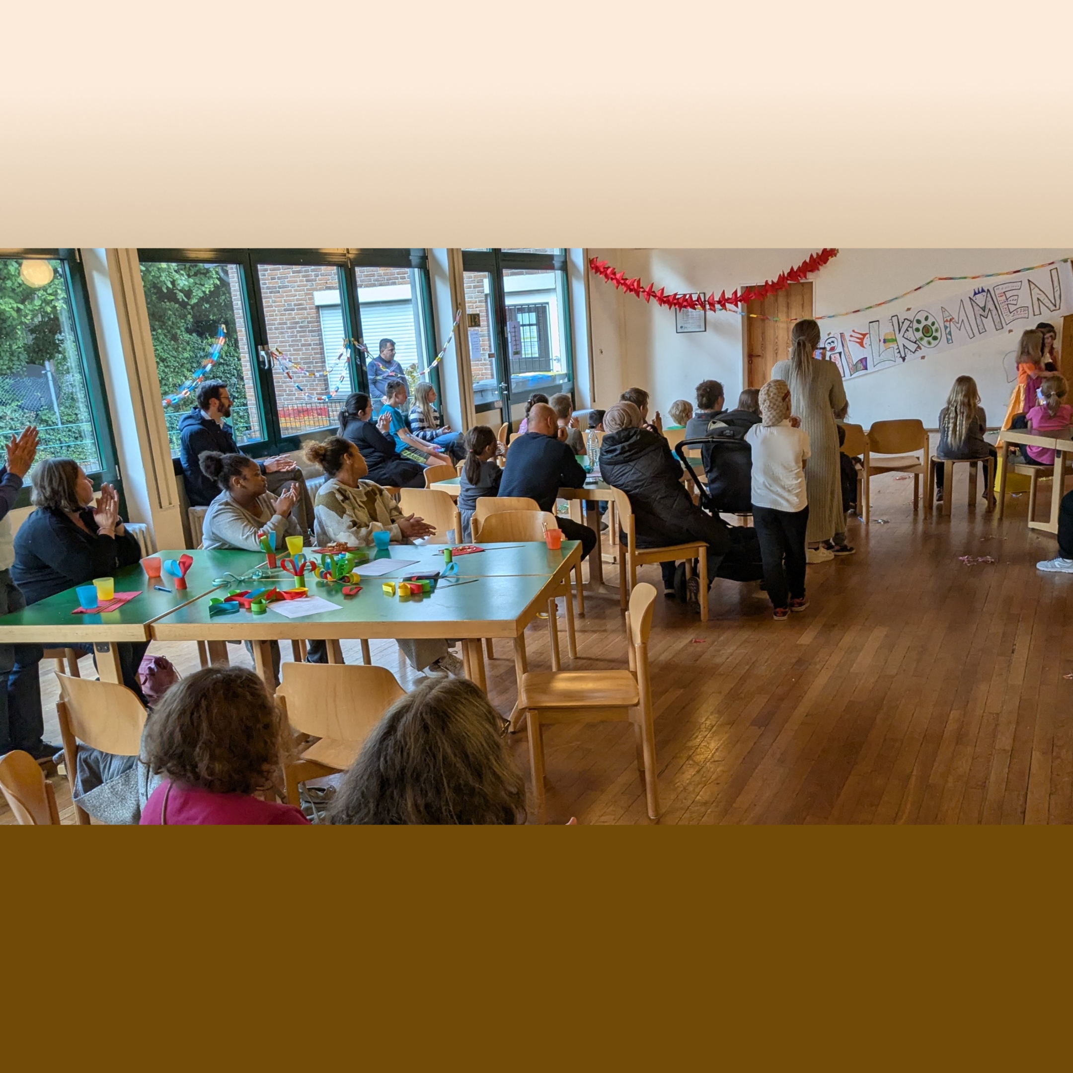 Menschen unterschiedlichen Alters sitzen an Tischen und schauen nach vorne zu einem Willkommens-Schild.