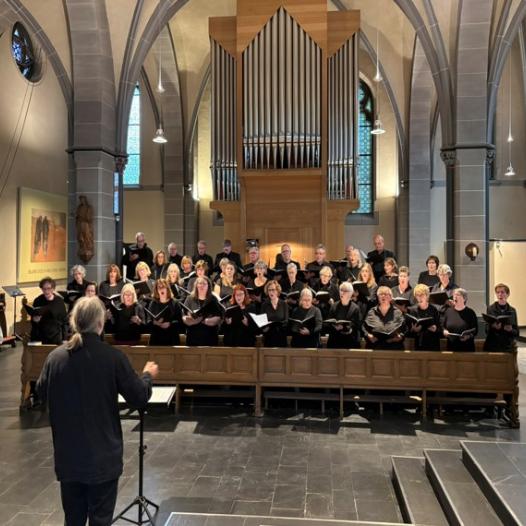 Chormitglieder stehen singend vor der St. Clemens-Orgel und singen gemeinsam. Im Vordergrund steht der Dirigent.